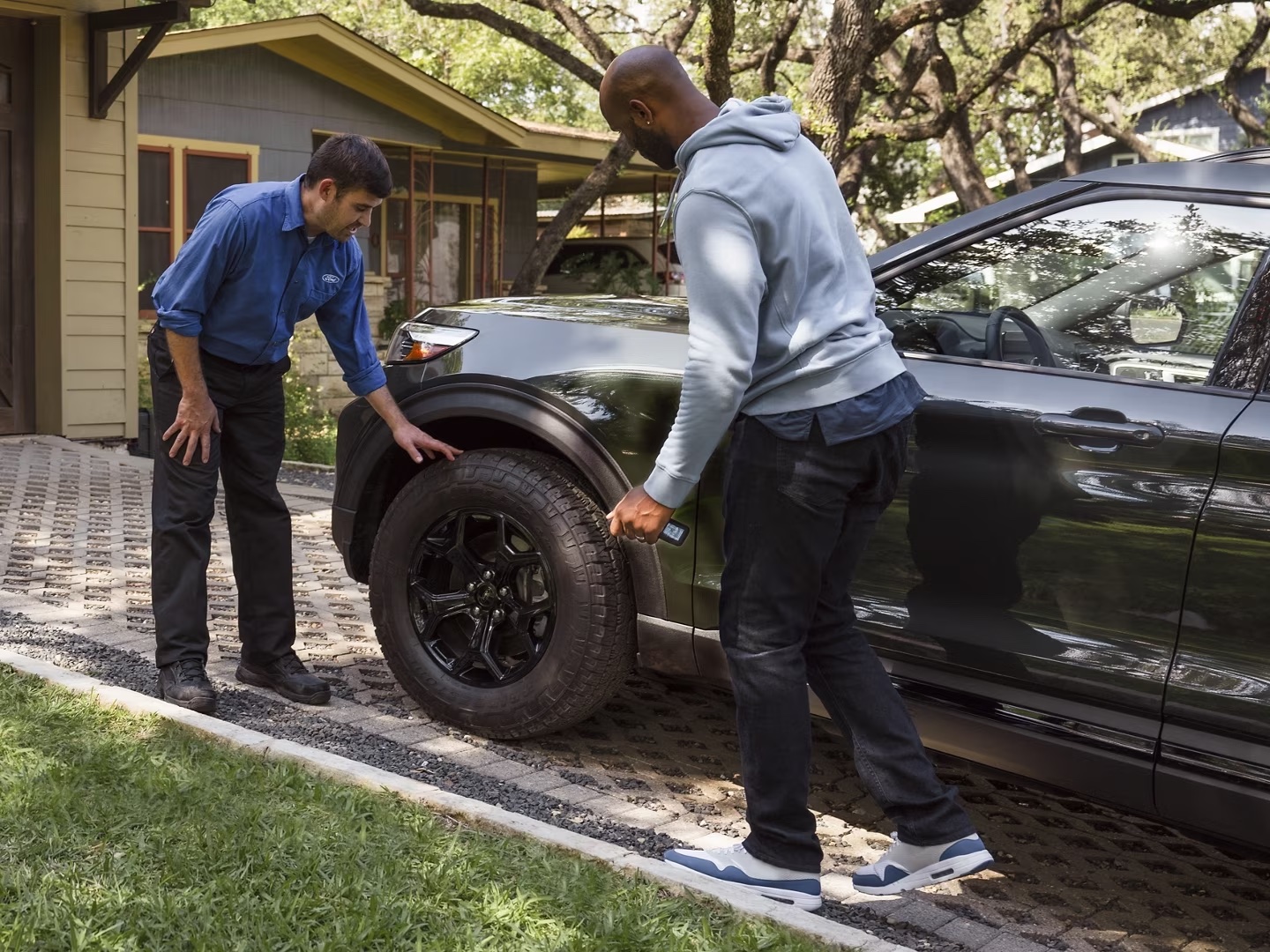 A Ford Service technician inspecting the tires of a vehicle outside of a drivers home