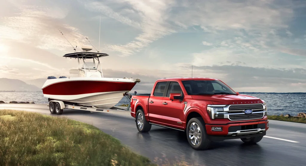 Red Ford F-150 towing a boat on a lake side road